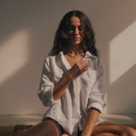 woman wearing linen shirt and heart necklace moving on a yoga mat with sunlight