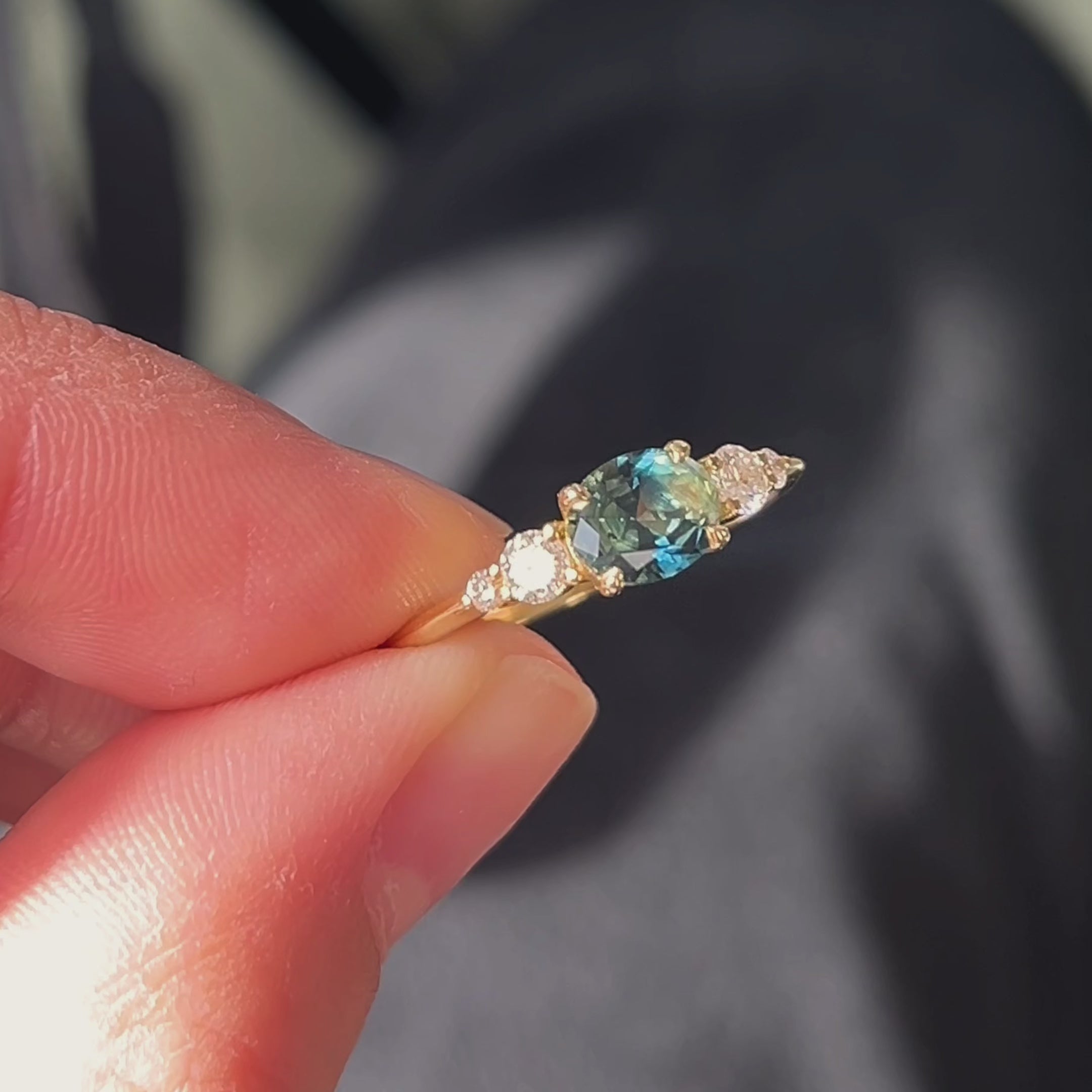 hand holding bi colour blue green sapphire engagement ring in the sun