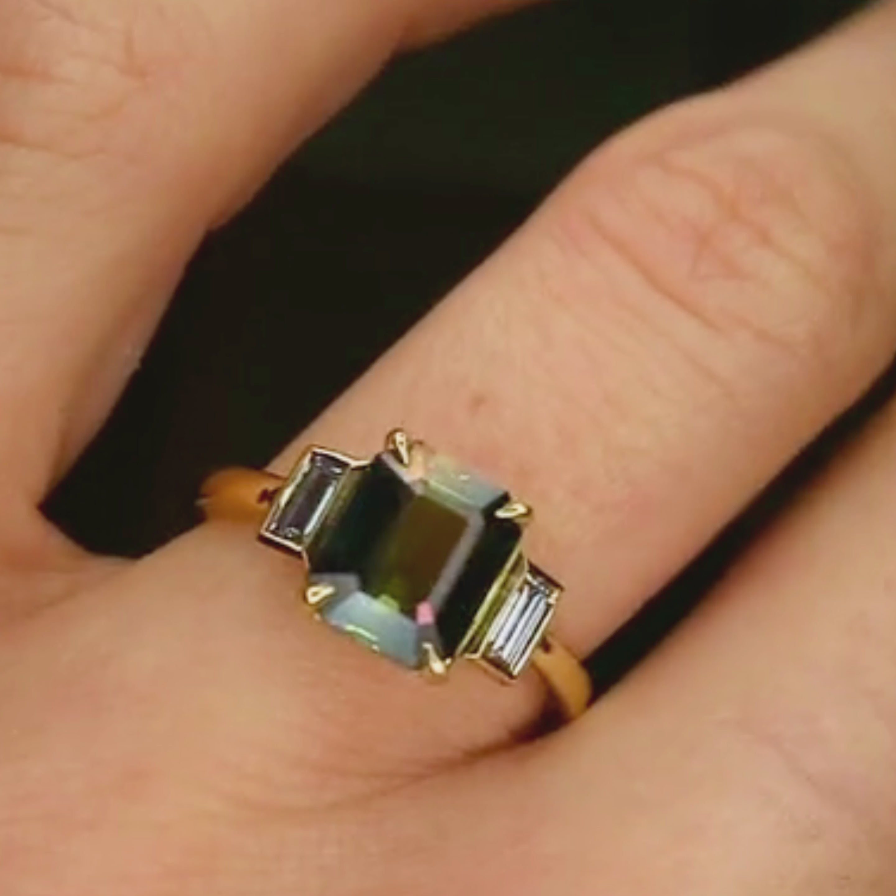 blue/green sapphire engagement ring with bezel baguette diamonds worn on a hand