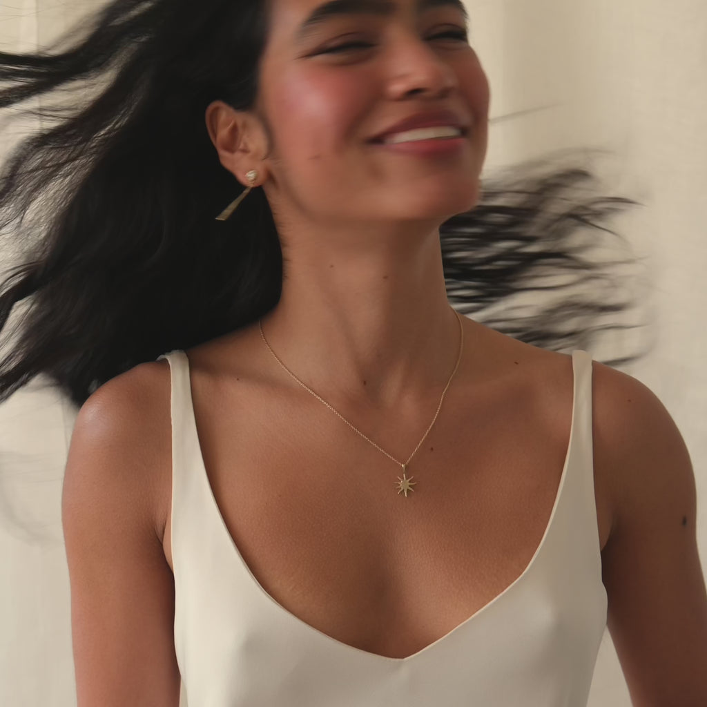 woman shaking her hair and smiling to camera wearing v neck wedding dress and gold jewellery