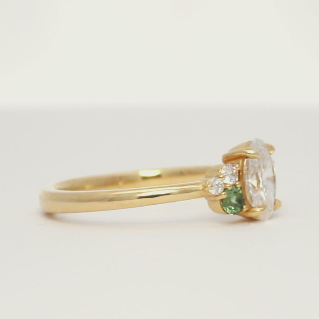 gold engagement ring with diamonds and small green sapphires spinning and sparkling on a turntable