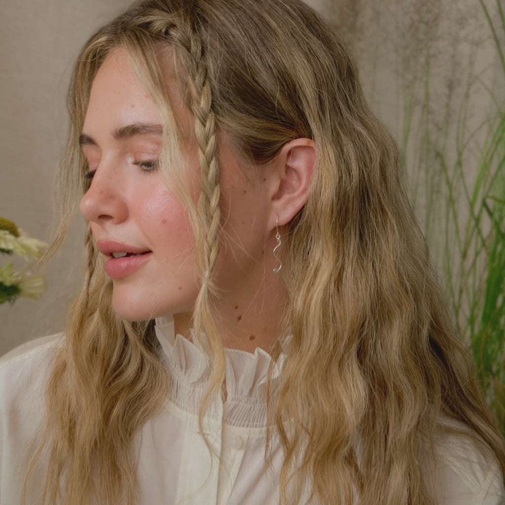 blonde model holding a flower with braided hair wearing some dainty wavy dangle earrings 