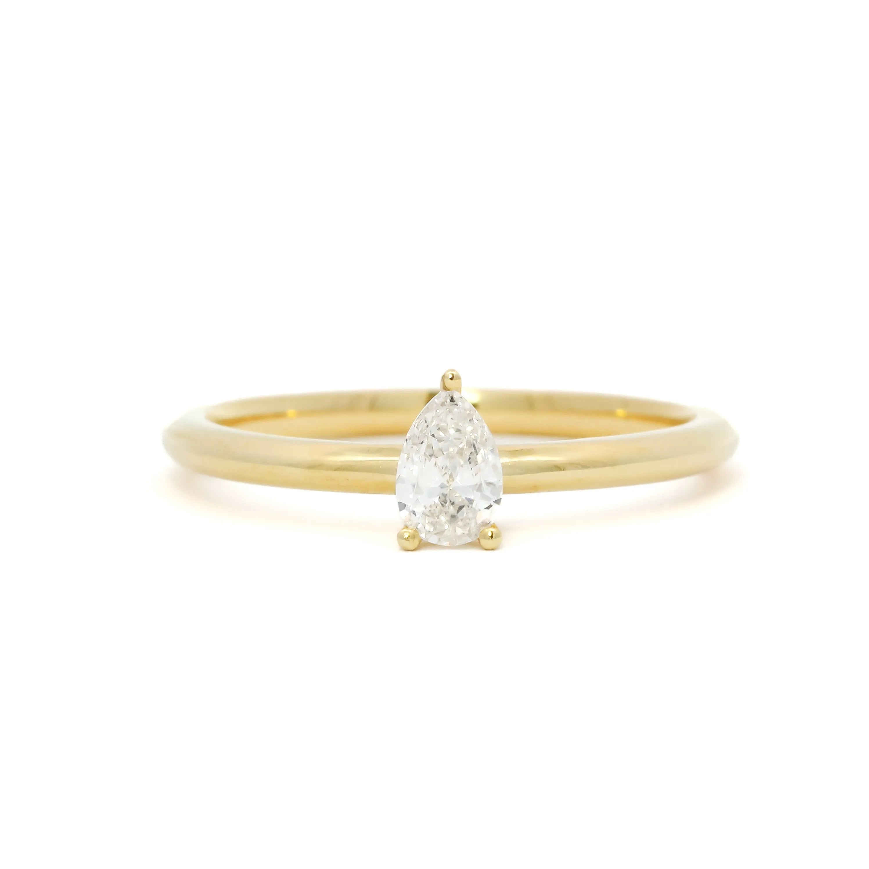 Gold dainty placeholder engagement ring with a small pear-shaped diamond on a white background
