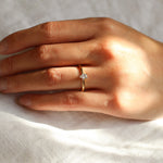 tiny diamond engagement ring on hand with the sun on a neutral fabric