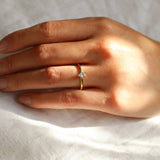 tiny diamond engagement ring on hand with the sun on a neutral fabric