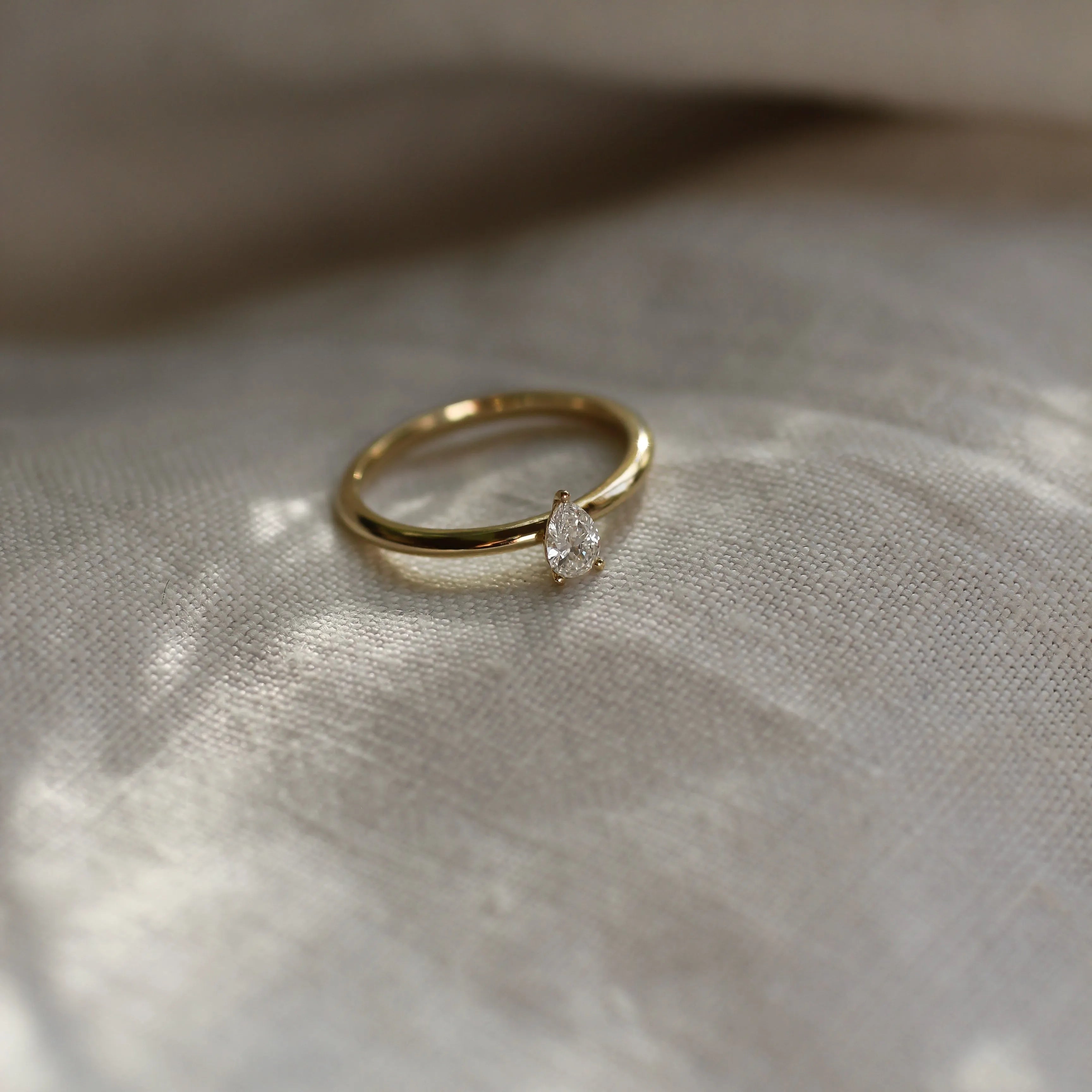 gold ring with small pear diamond on a neutral fabric and blurred background