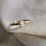 small pear diamond solitaire engagement ring on a textured neutral fabric and blurred background