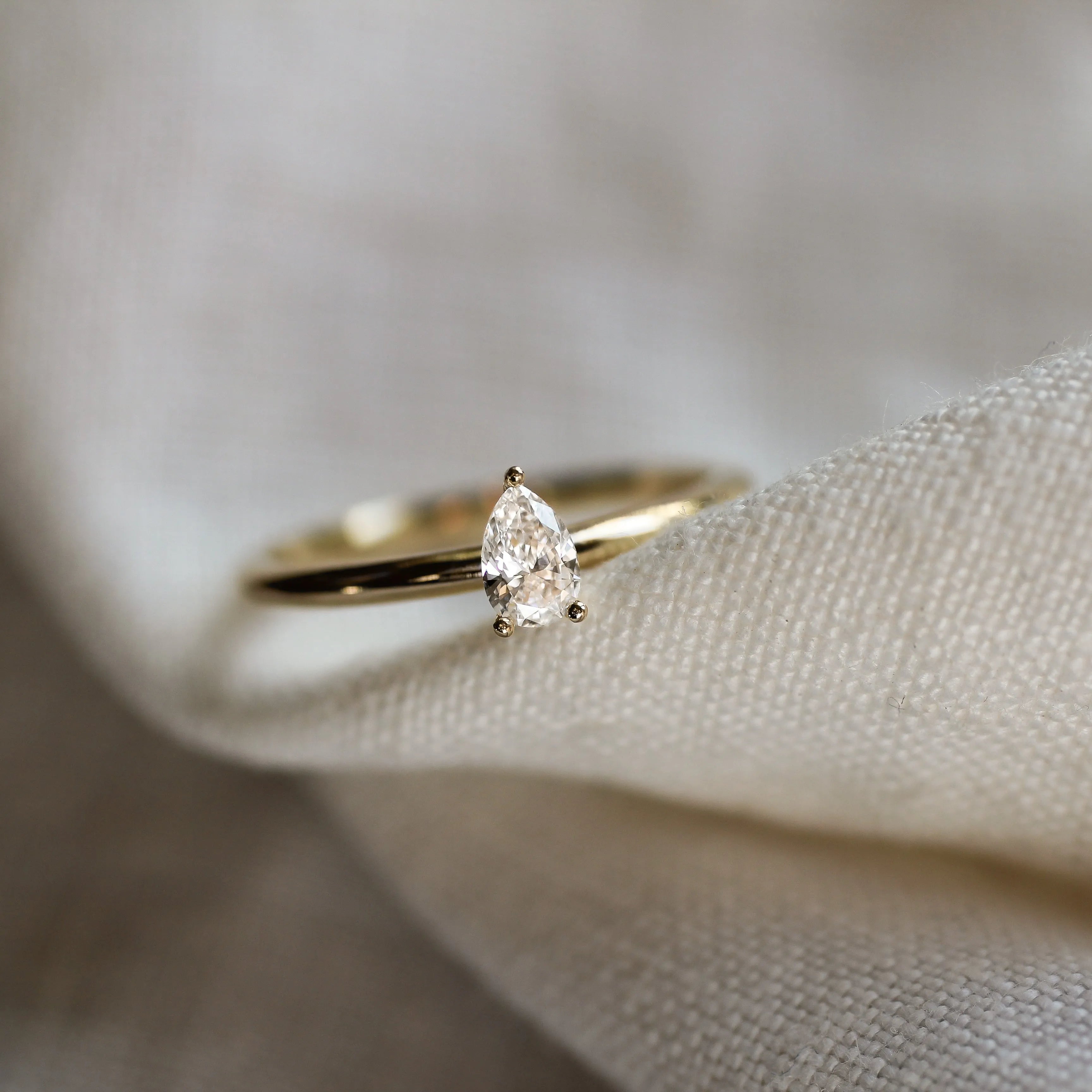 small pear diamond solitaire engagement ring on a textured neutral fabric and blurred background