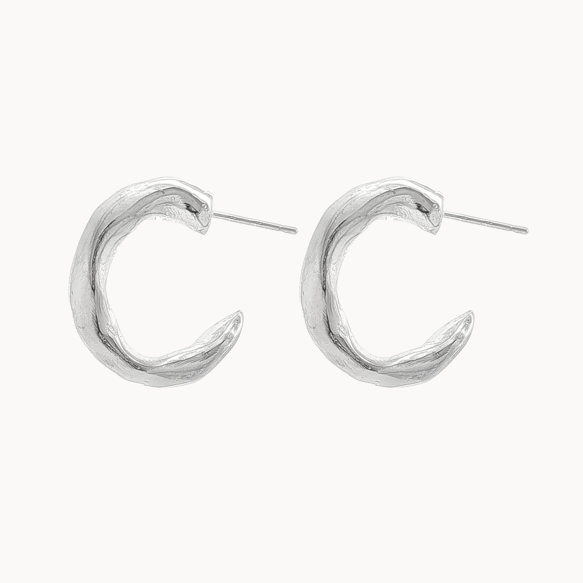 A pair of textured silver crescent hoop earrings with post backs, displayed on a clean off-white background.