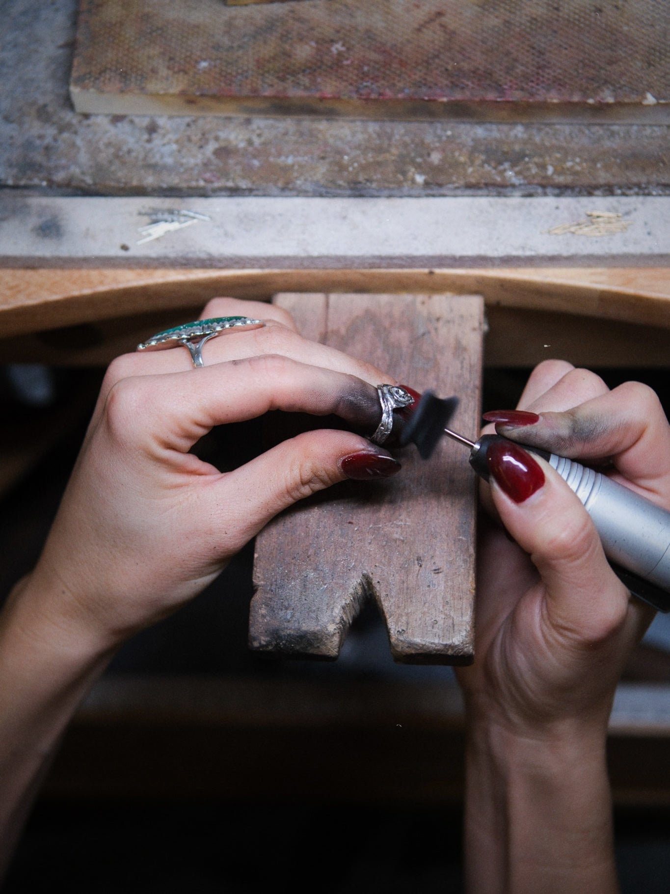 Person working on a piece of jewelry with a tool on a wooden block.