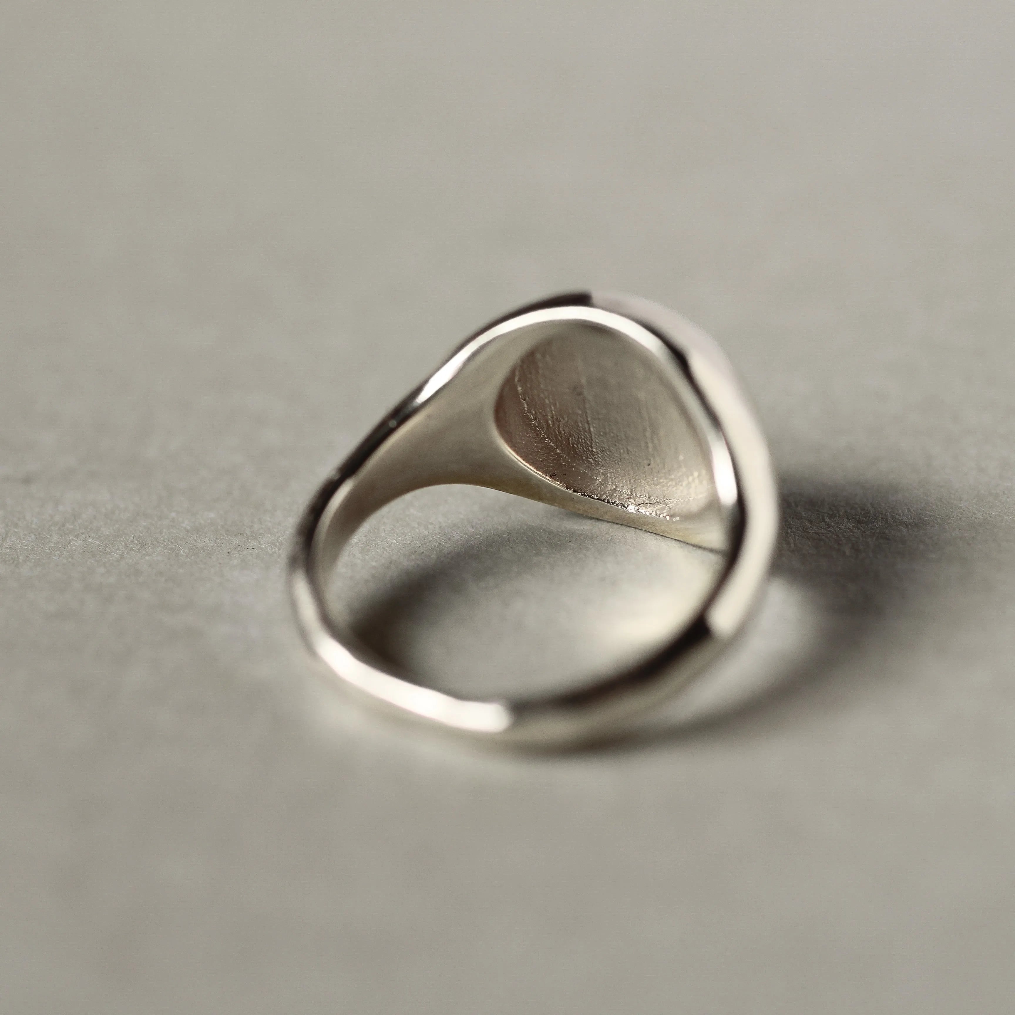 back view of silver signet ring on beige surface