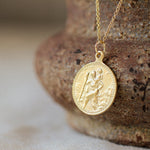 gold saint christopher necklace with round embossed pendant and gold chain against a brown textured bowl