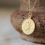 gold saint christopher necklace with round embossed pendant and gold chain against a brown textured bowl