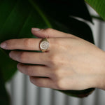 Hand wearing a gold saint christopher signet ring with a leafy background