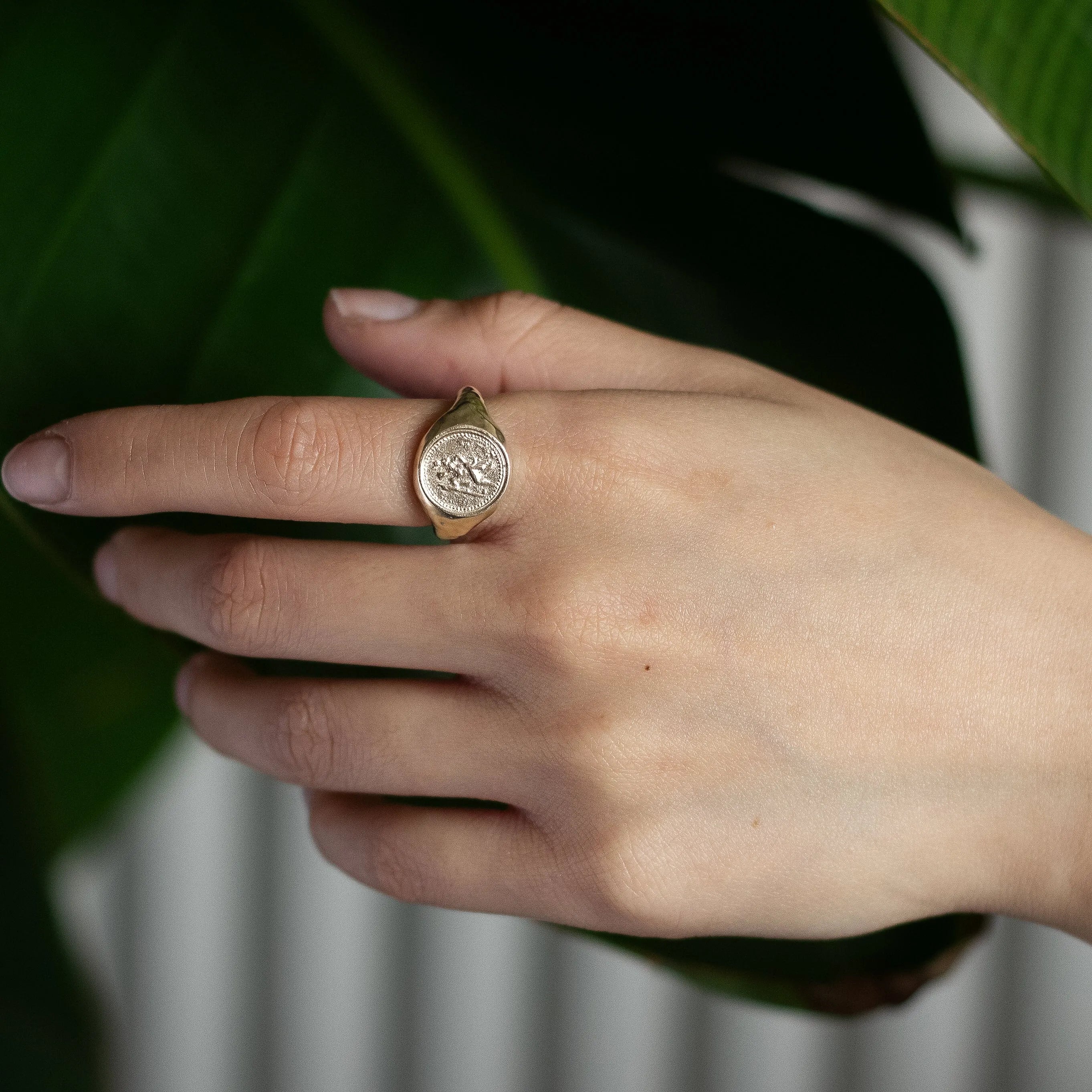 Hand wearing a gold saint christopher signet ring with a leafy background
