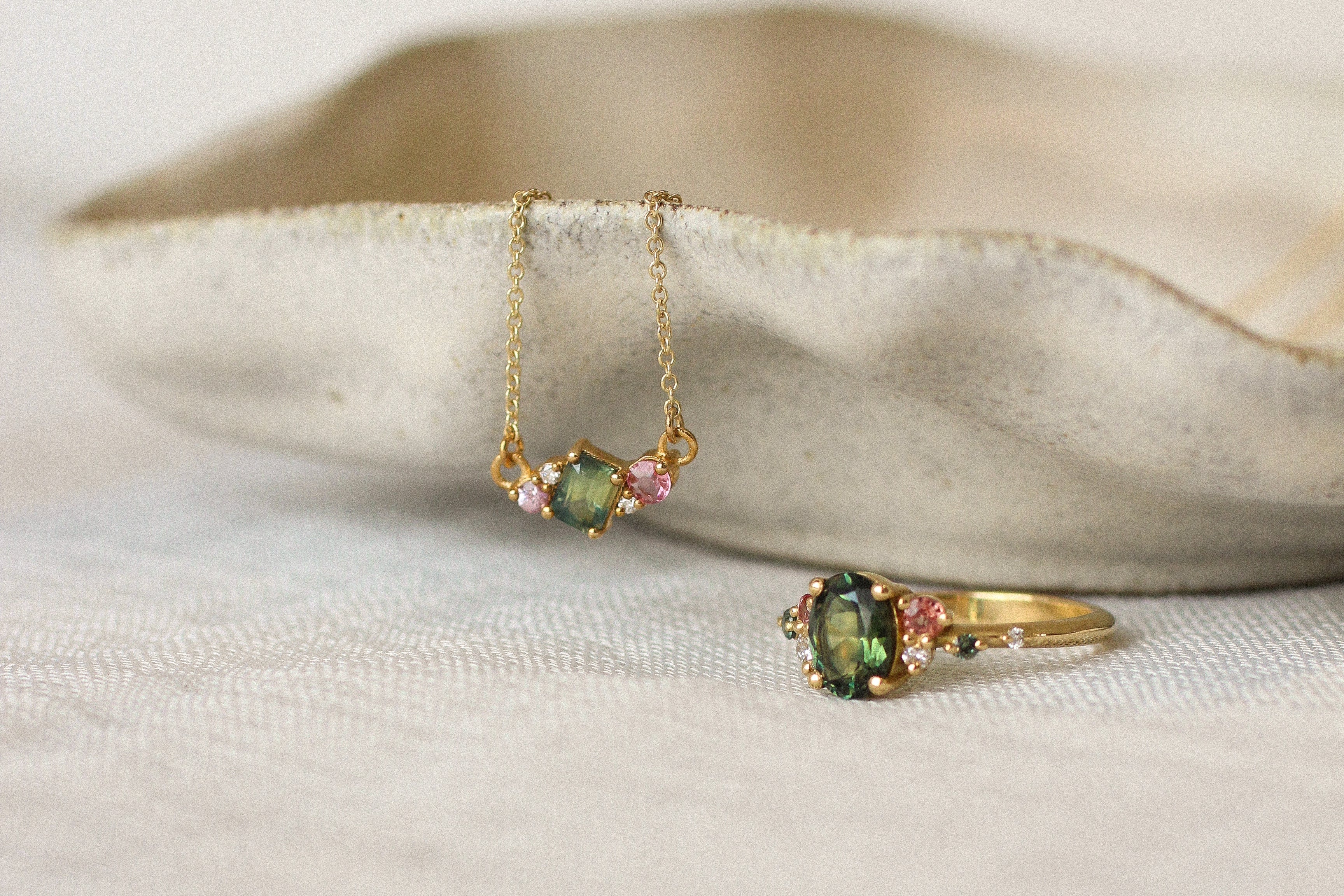 Gold necklace and ring with green gemstones on a beige dish.