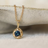 Gold necklace with a blue gemstone pendant on a neutral background