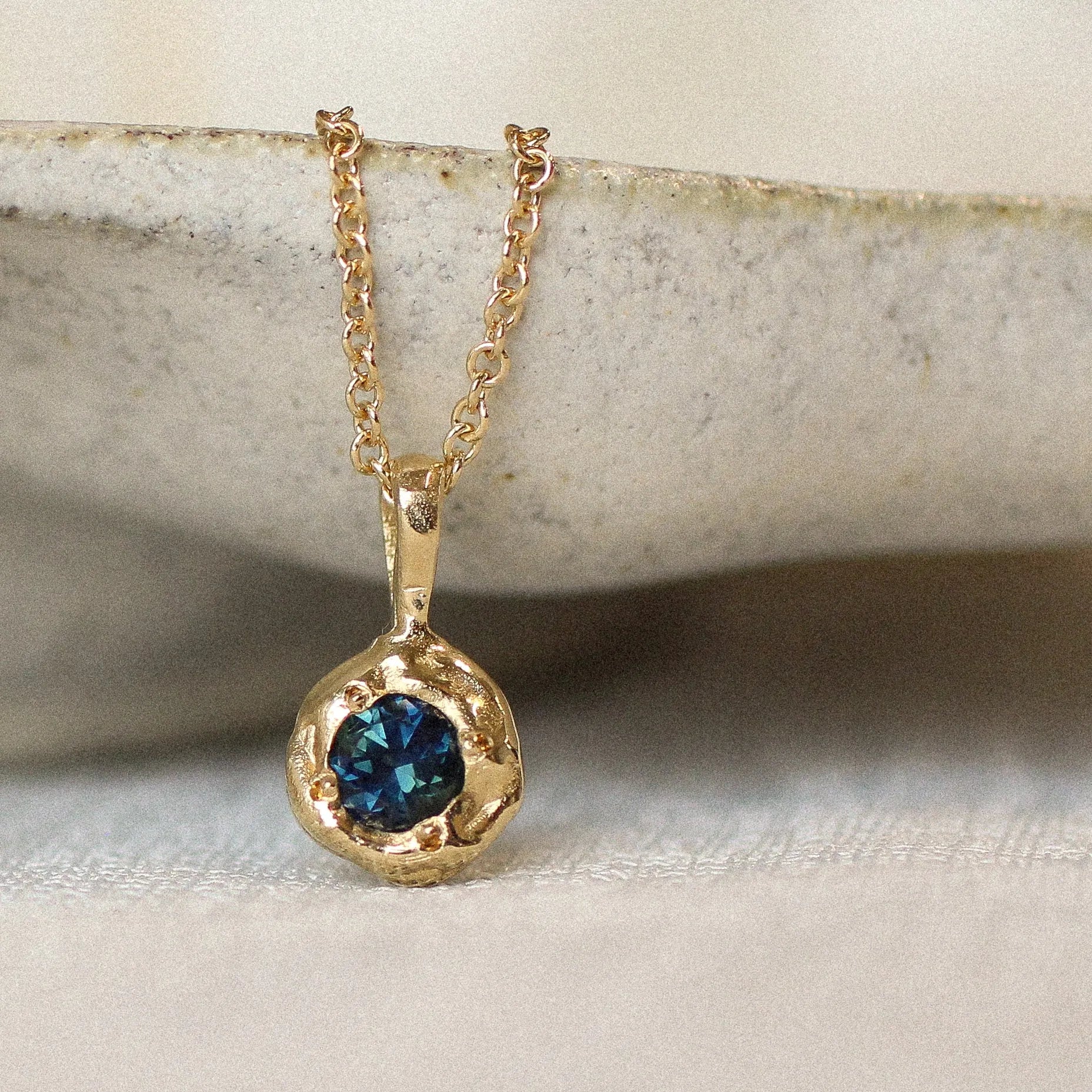 Gold necklace with a blue gemstone pendant on a neutral background