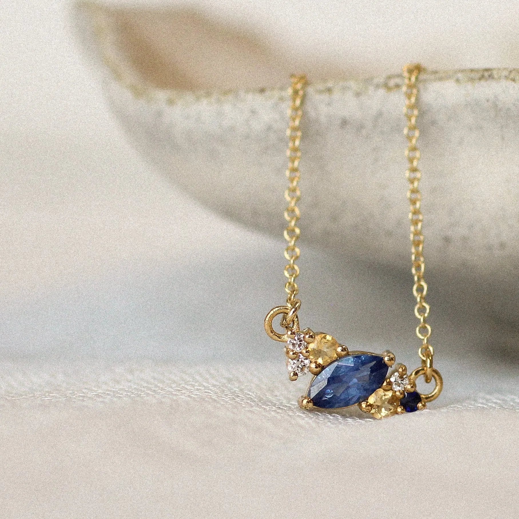 cluster gemstone necklace with marquise-cut blue sapphire, small yellow sapphires and diamonds resting on a ceramic surface