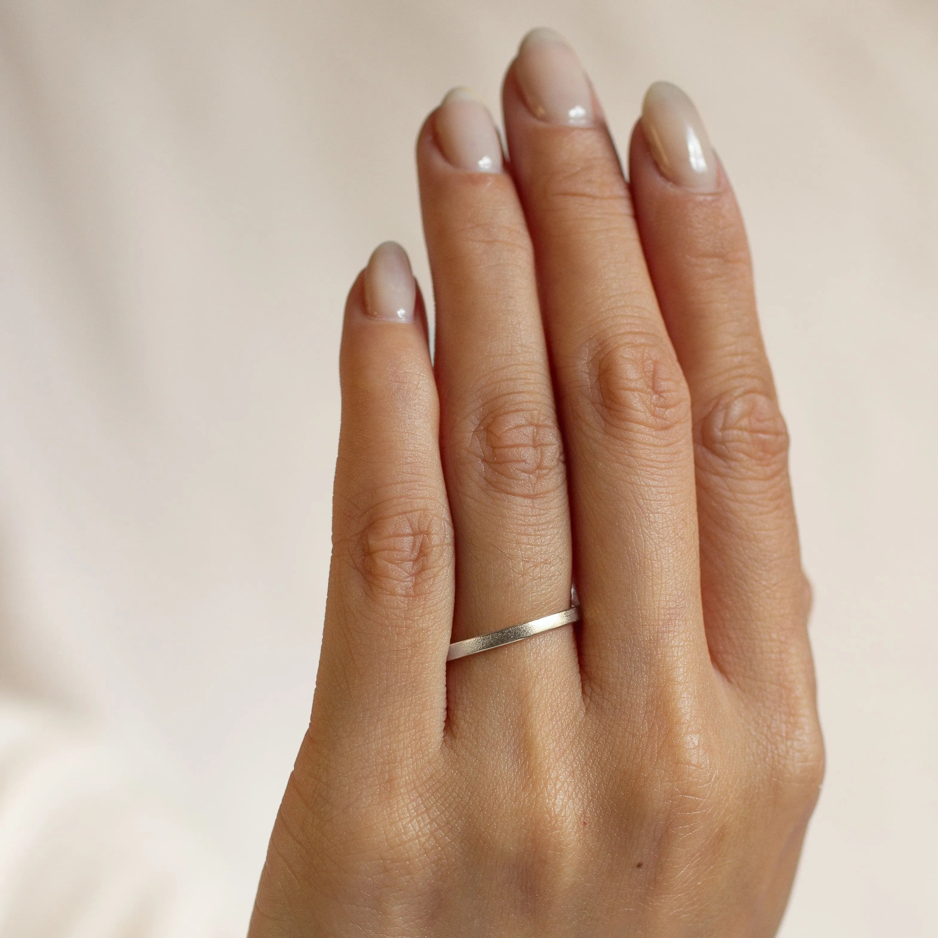 Hand wearing a 2mm flat satin finish wedding ring in white gold on a neutral background