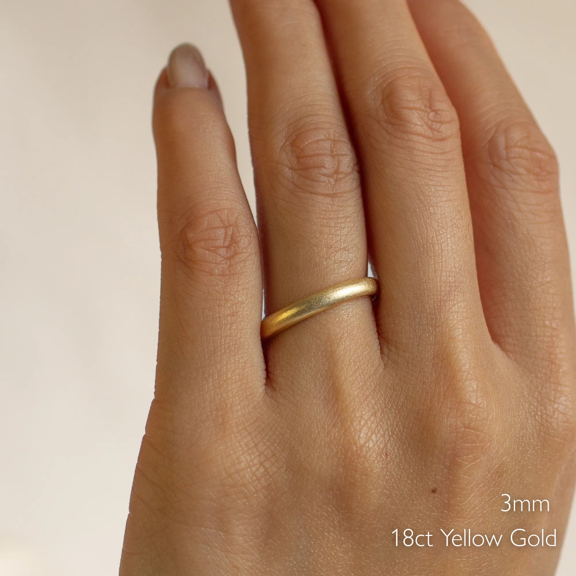 Gold satin wedding ring on a hand with '3mm 18ct Yellow Gold' text
