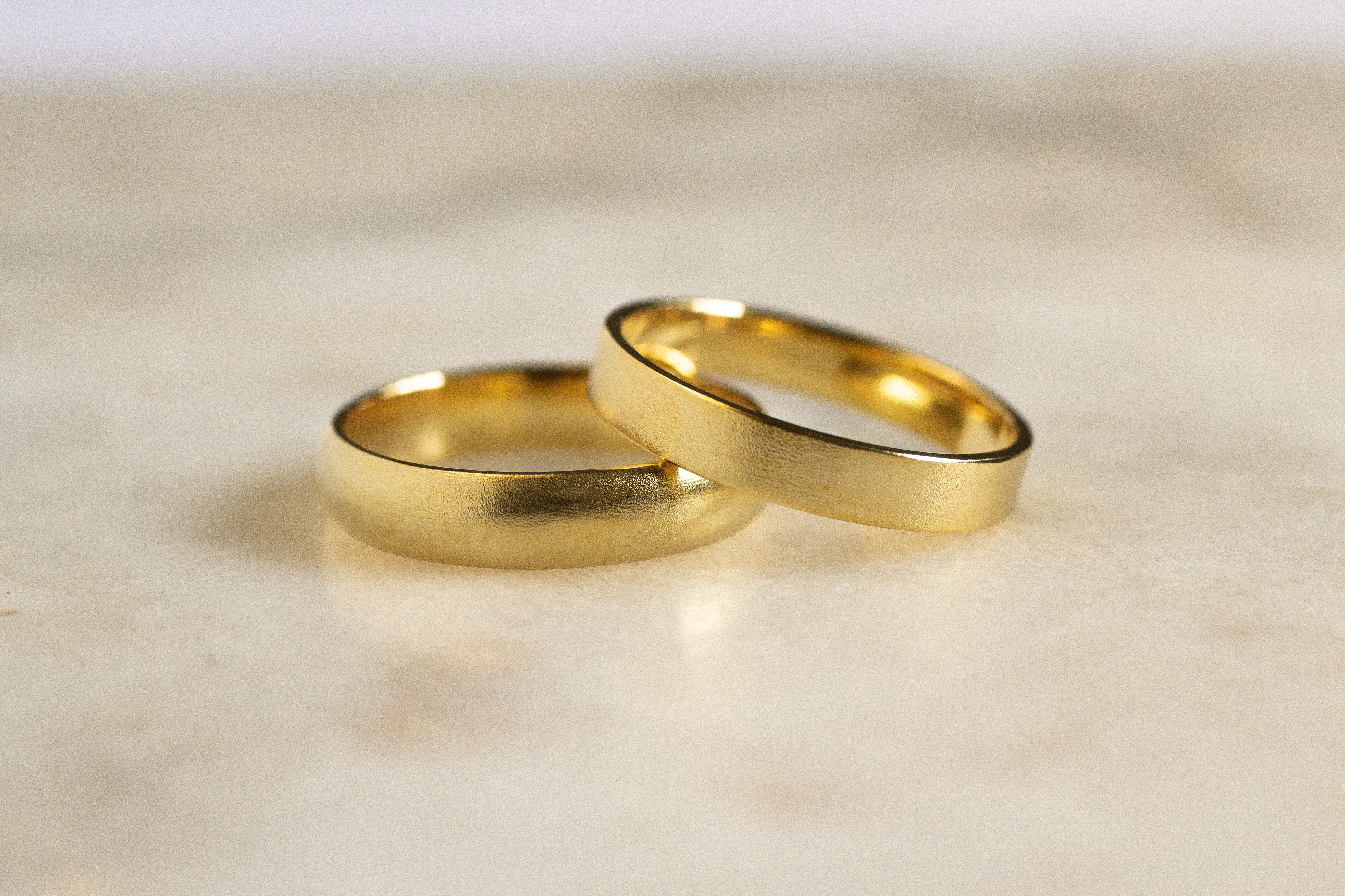 wedding rings with satin blurred texture in flat and d shapes leaning on one another on a marble surface