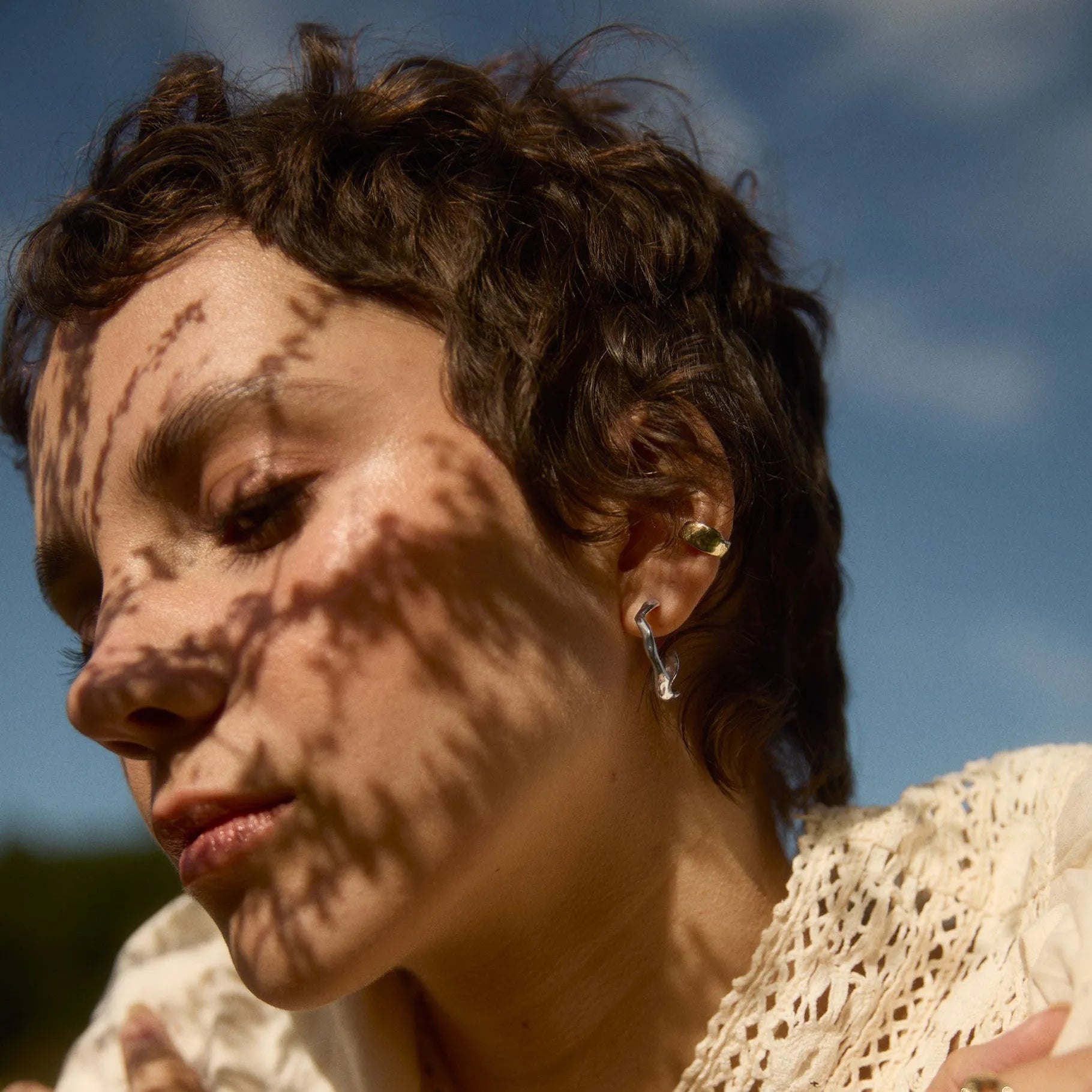 model with shadow of flowers on face wearing silver wave hoop earrings and gold ear cuff