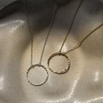 necklace with open hammered circle pendant in silver and gold on a textured ceramic dish