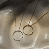 necklace with open hammered circle pendant in silver and gold on a textured ceramic dish