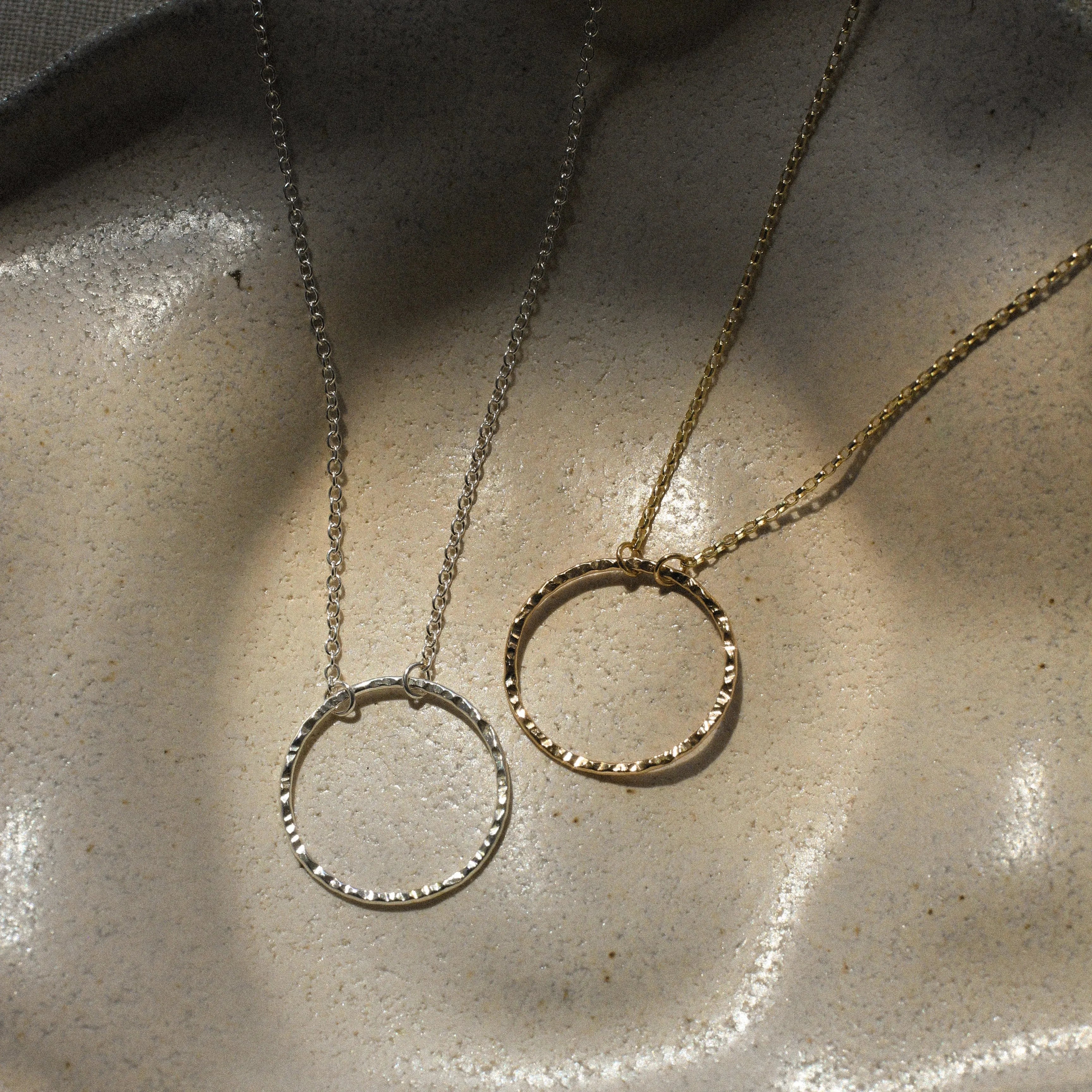 necklace with open hammered circle pendant in silver and gold on a textured ceramic dish