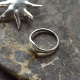 close up of a silver signet ring with sun-shaped earring in the background on a grey marbled surface
