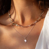 Close-up of a person wearing a silver leaf chain necklace with a star pendant.