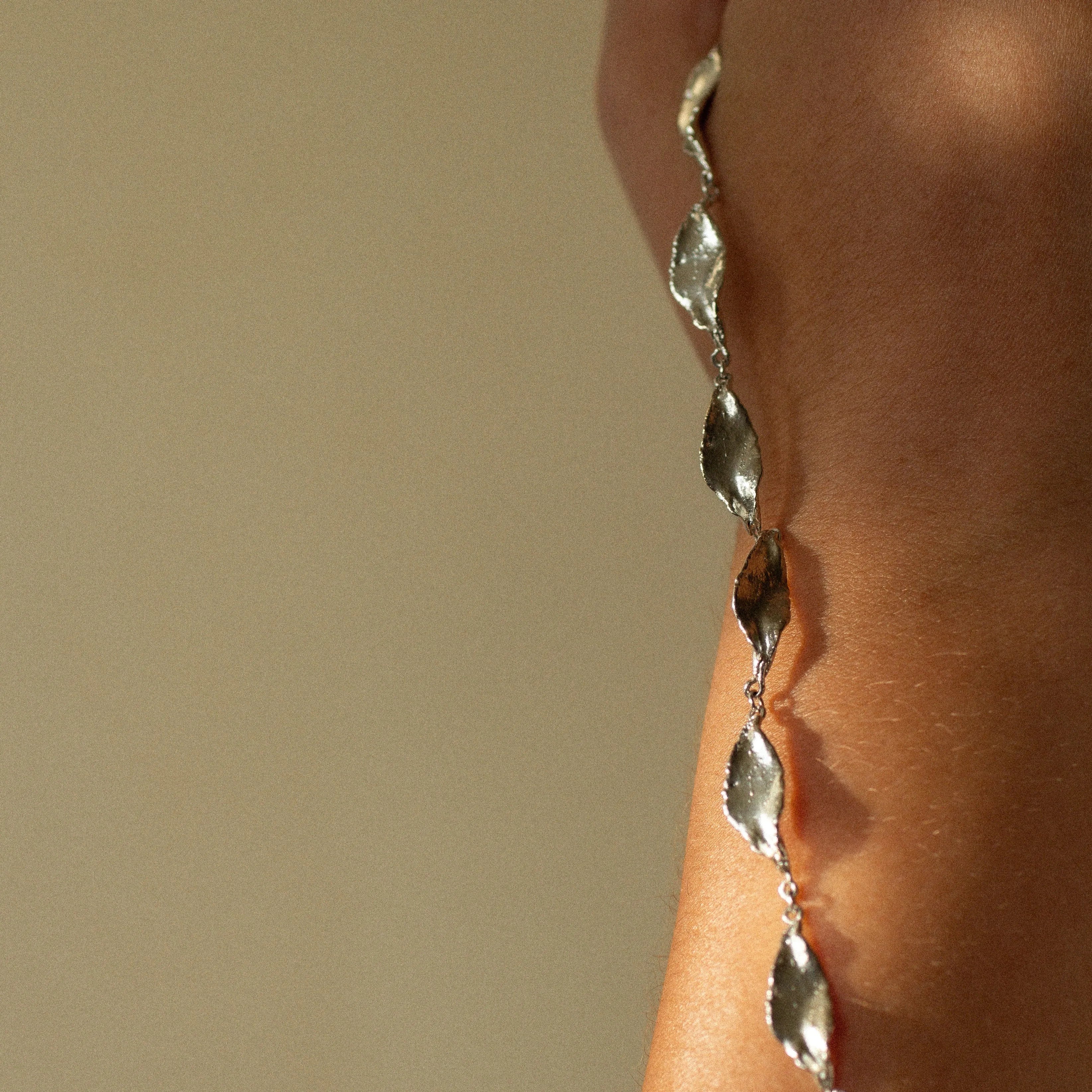 close up of silver chain leaf necklace hanging on arm