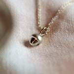 Silver necklace with a acorn-shaped pendant on a soft fabric background