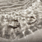 mini silver hoop earrings on a beige surface and reflective glass pattern