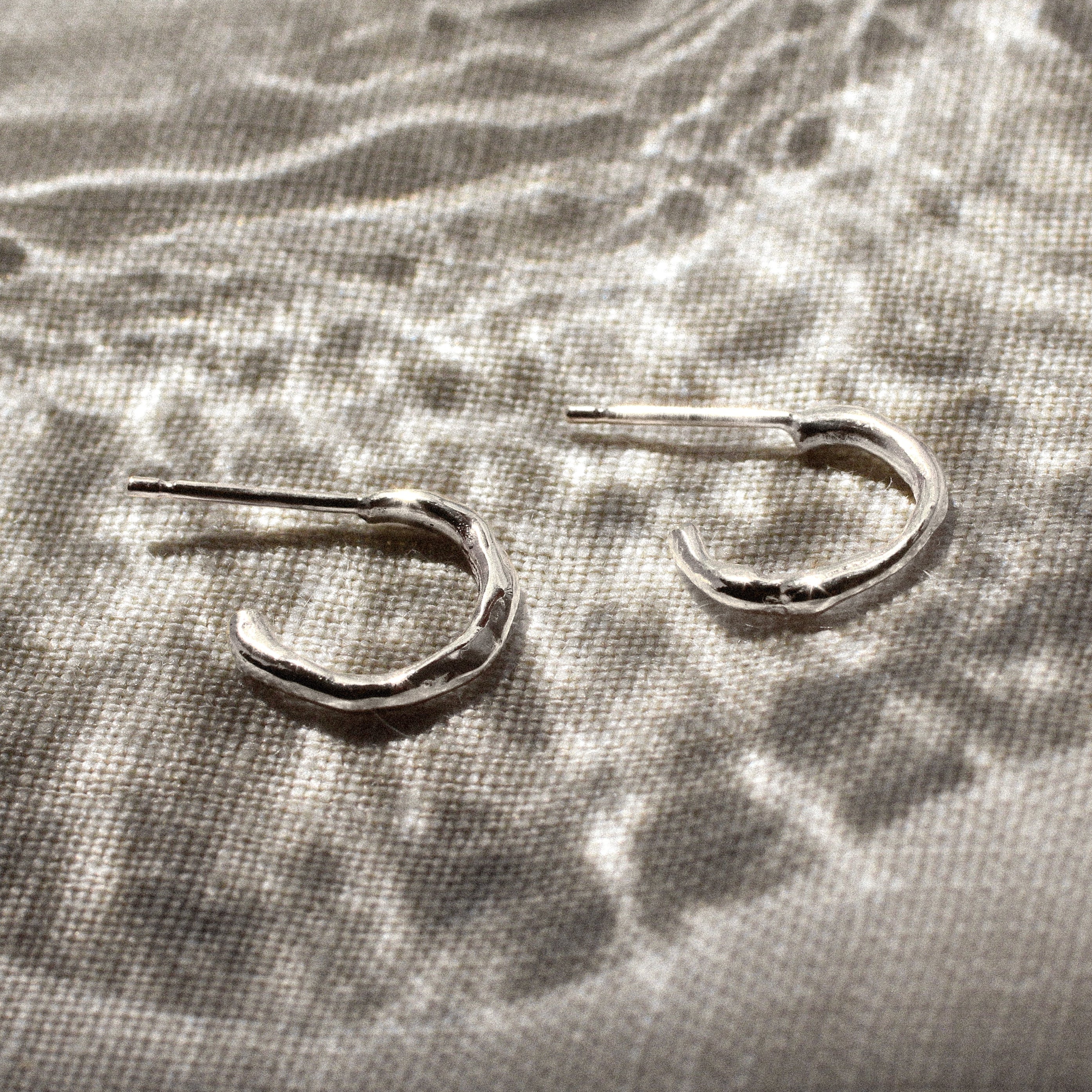 mini silver hoop earrings on a beige surface and reflective glass pattern