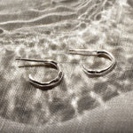 mini silver hoop earrings on a beige surface and reflective glass pattern