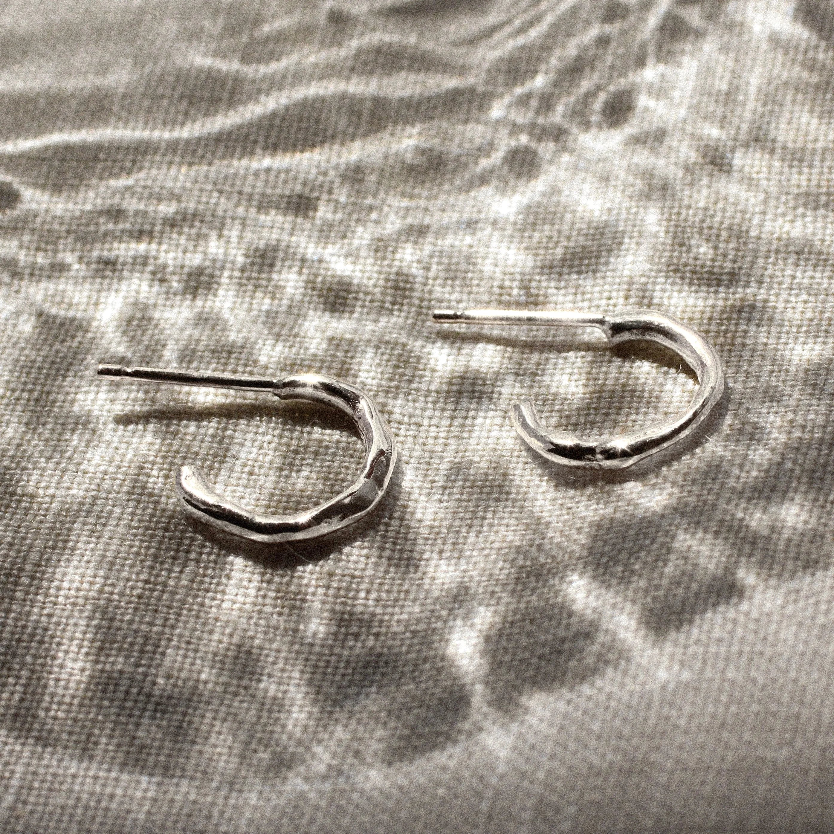 mini silver hoop earrings on a beige surface and reflective glass pattern