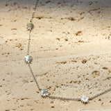 Silver necklace with sun-shaped pendants on a textured beige surface
