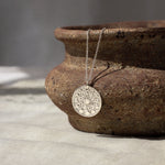 silver necklace with moonphase pendant hanging from a textured brown ceramic dish