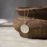 silver necklace with moonphase pendant hanging from a textured brown ceramic dish