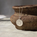 silver necklace with moonphase pendant hanging from a textured brown ceramic dish