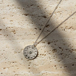 silver necklace with round pendant and moonphase design on a stone textured surface with shadows