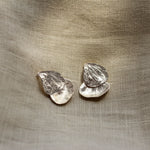 Pair of silver petal-shaped earrings on a textured beige fabric background