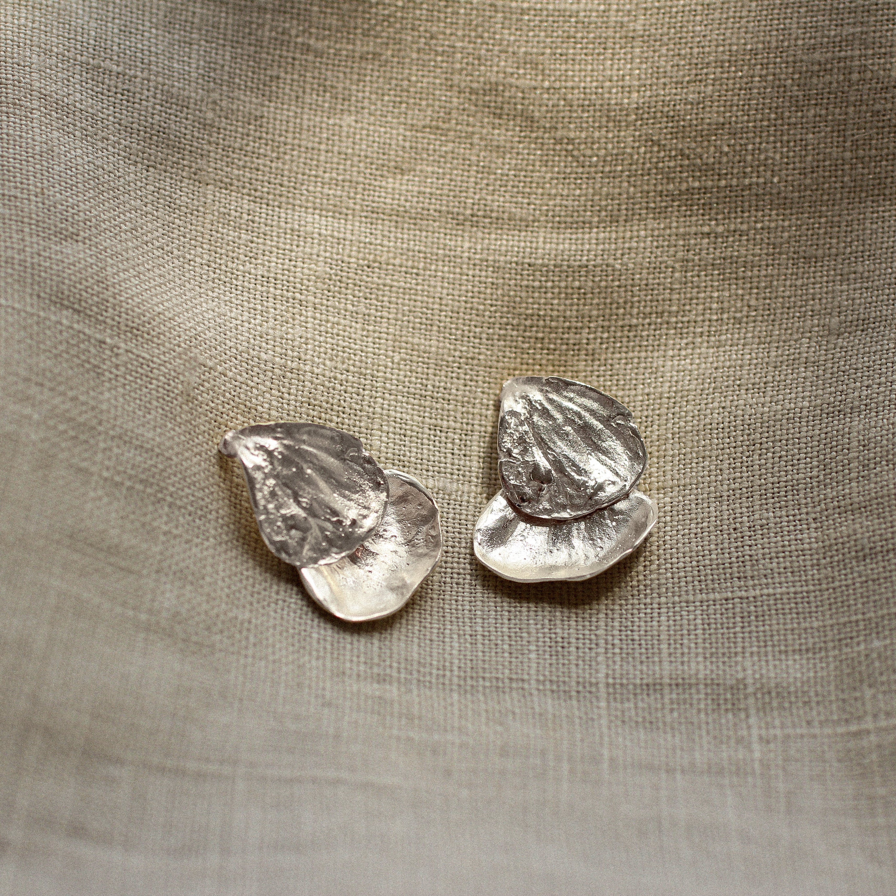 Pair of silver petal-shaped earrings on a textured beige fabric background