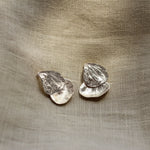 Pair of silver petal-shaped earrings on a textured beige fabric background