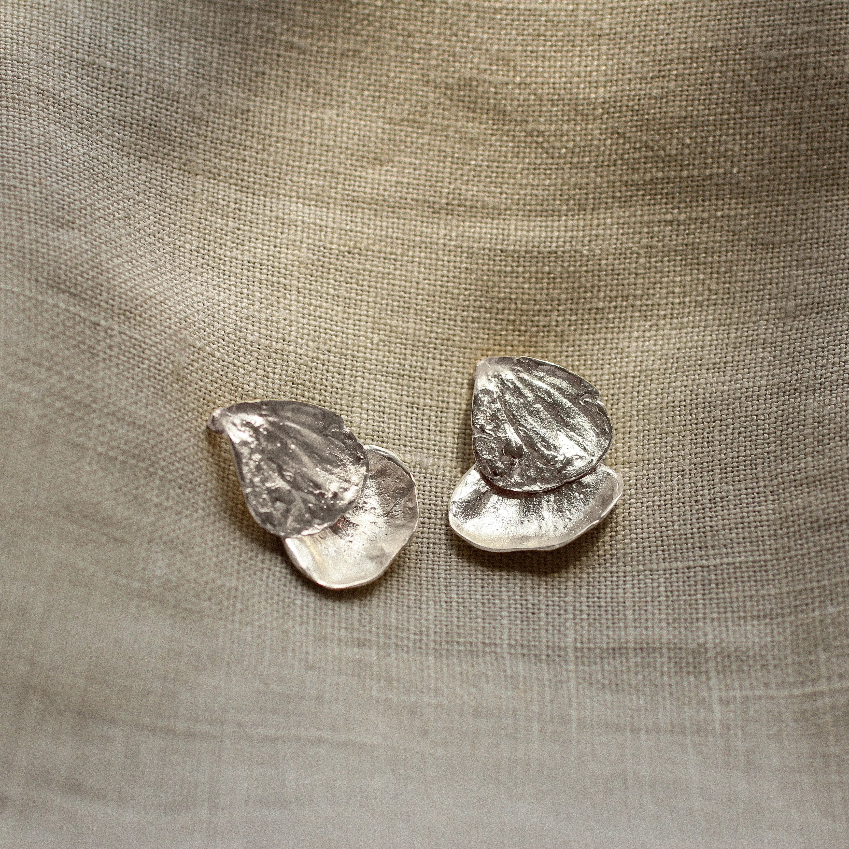 Pair of silver petal-shaped earrings on a textured beige fabric background