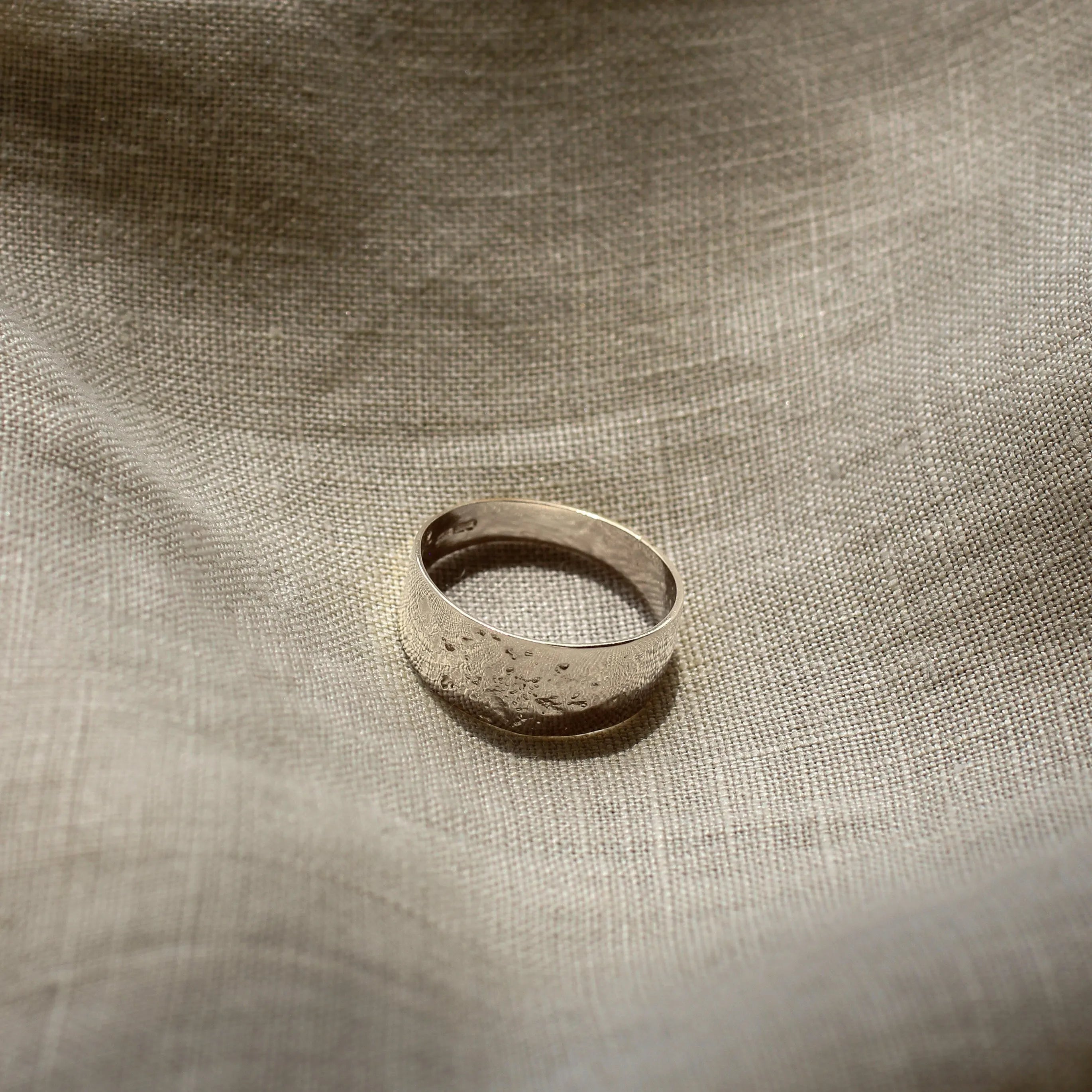 Silver ring on a textured beige fabric surface
