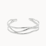 A silver open cuff bracelet with a wavy, organic textured design, photographed on a clean off-white background.