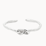 A textured sterling silver open cuff bangle featuring a central knotted design, shown on a plain off-white background.